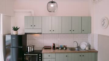 A kitchen with light green cabinets, a black refrigerator, a stove, and a sink.