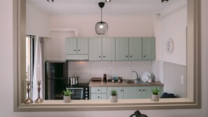 Une cuisine moderne avec des meubles de couleur vert clair, un réfrigérateur noir, un four encastré et un luminaire suspendu.