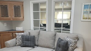A living room with a sectional sofa, a wooden coffee table, and a view of the outdoors through large windows. - Minutes to the Beach with a hot tub and decks for relaxing. (Ocean View)
