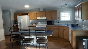 A modern kitchen with wooden cabinets, a built-in oven, a refrigerator, and a dining area with chairs. - Minutes to the Beach with a hot tub and decks for relaxing. (Ocean View)