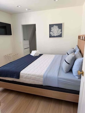 A bedroom with a bed, a bedside table, a wall-mounted TV, a framed picture, and a door leading to a bathroom. - 2.5 blocks from Beach in Lower Chelsea area of A.C (Atlantic City)