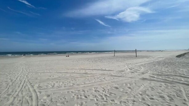 En bred, sandet strand med fodspor og en klar, blå himmel.