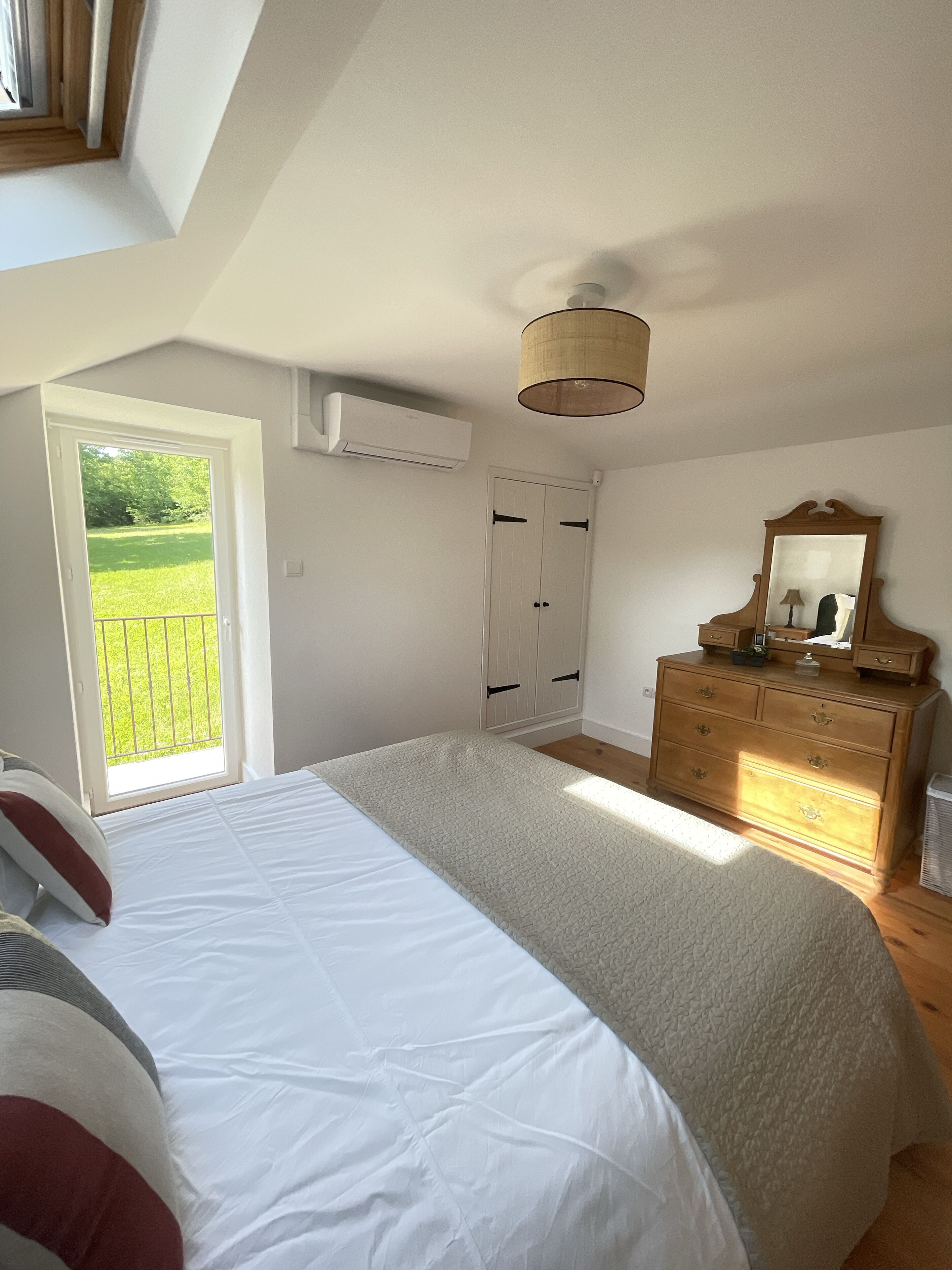 A bedroom with a large bed, a dresser, a mirror, and a door leading to a balcony.