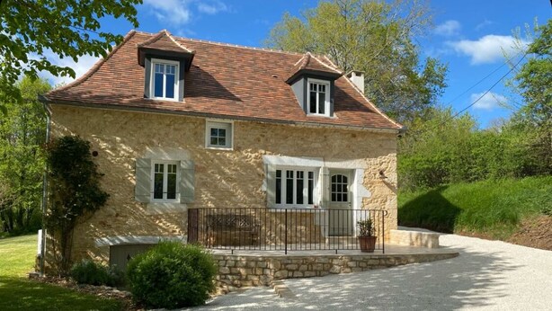 Una casa de piedra con camino de grava, dos ventanas y un pequeño porche.
