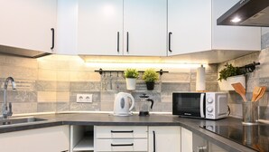 A modern kitchen with white cabinets, a stainless steel sink, a microwave, and a kettle. - Moderno y elegante ap. Barrio Ibiza MEN30 (Madrid)