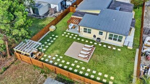 A residential backyard with a house, a fenced area, and a patio with seating.