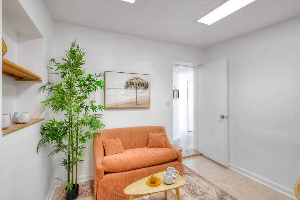 A room with a sofa, a small table with a cup and saucer, a potted plant, and a painting on the wall.