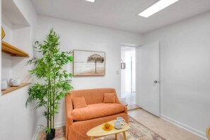 A room with a sofa, a small table with a cup and saucer, a potted plant, and a painting on the wall. - Surf Shack! Pool table! Fire Pit! 10 min to beach! (Martin County)