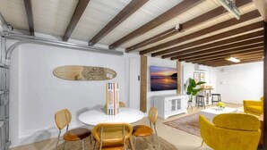 A modern interior with a dining area, yellow chairs, a white table, and a TV displaying a sunset.