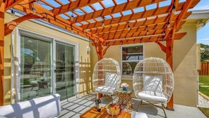 A covered outdoor seating area with wicker chairs, a sofa, and a table with a bottle and fruit. - Surf Shack! Pool table! Fire Pit! 10 min to beach! (Martin County)