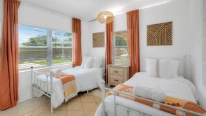 A hotel room with two beds, a window with curtains, a bedside table, and decorative wall panels.