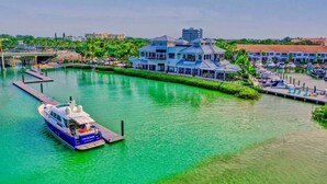 A marina with a yacht docked at a pier, a large building with a blue roof, and a clear view of the water. - Surf Shack! Pool table! Fire Pit! 10 min to beach! (Martin County)
