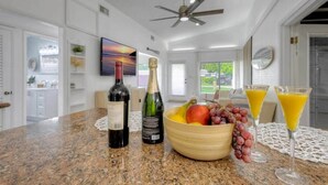 A kitchen with a granite countertop, a bottle of wine, a bottle of champagne, a bowl of fruit, and two glasses of orange juice. - Surf Shack! Pool table! Fire Pit! 10 min to beach! (Martin County)