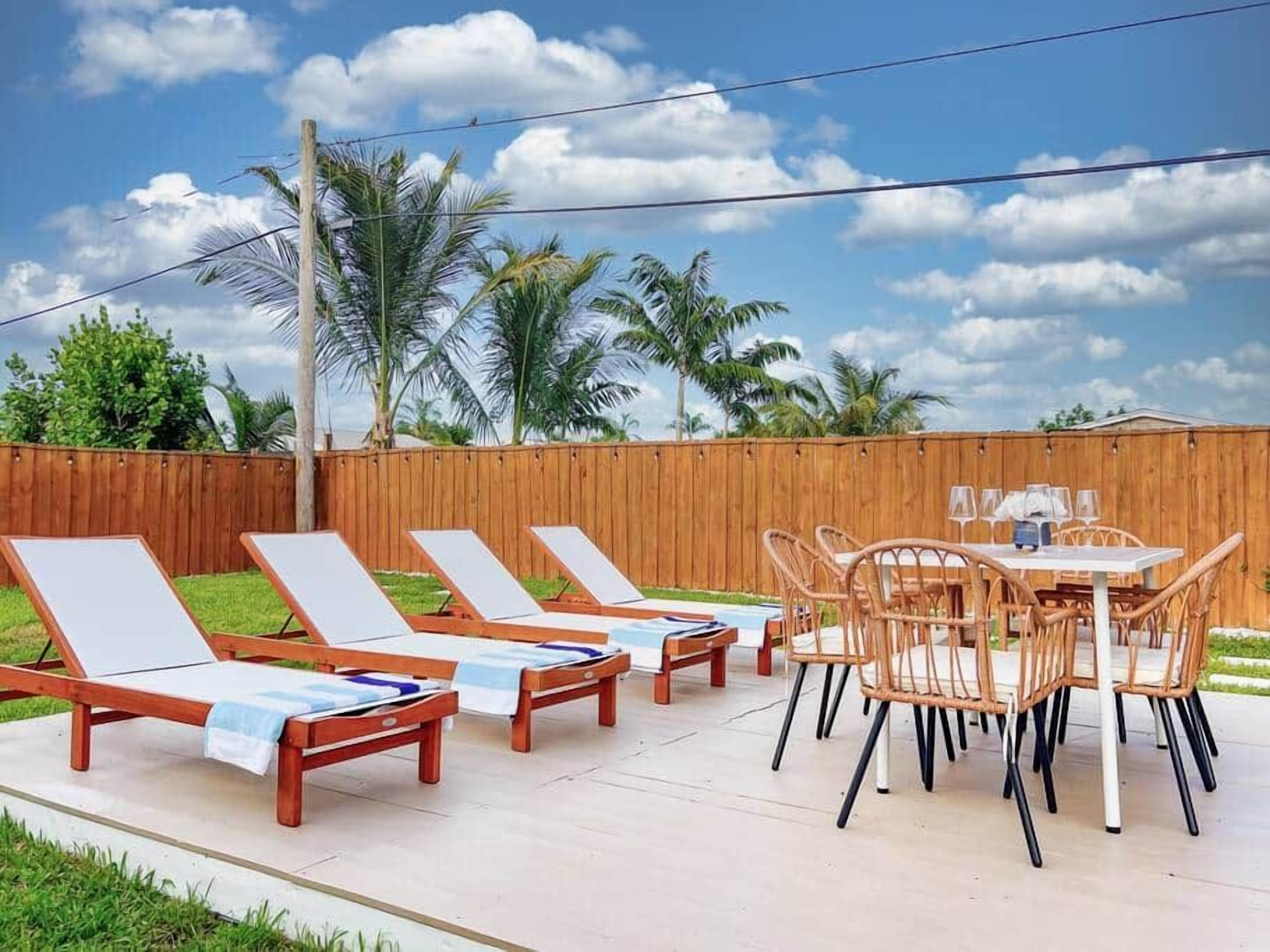 Eine Terrasse mit Holzliegen und einem Tisch mit Stühlen, umgeben von einem Holzzaun und Palmen.