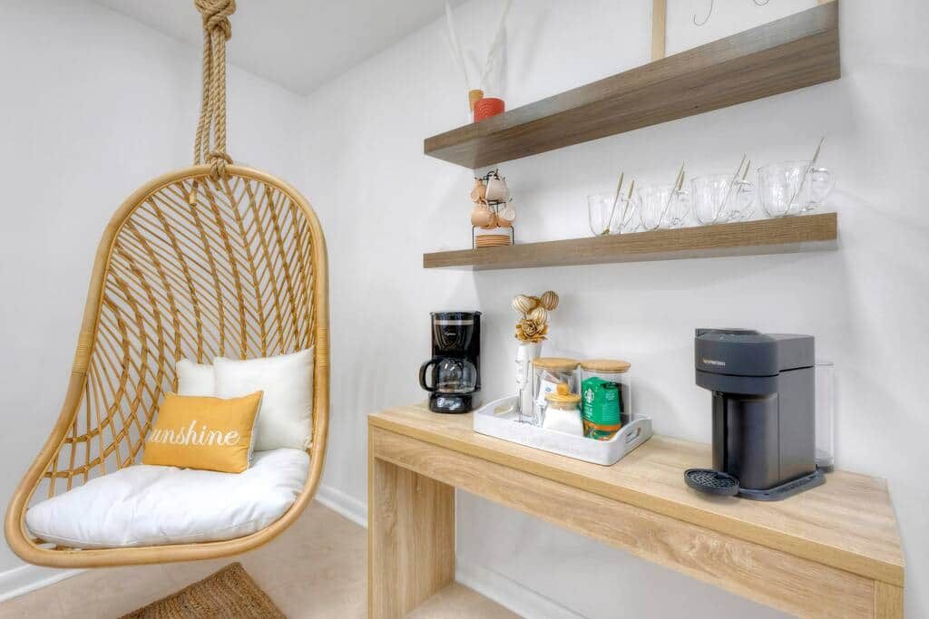 A room with a hanging chair, a coffee station, and shelves with glassware.