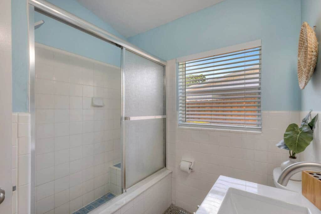 Ein Badezimmer mit Dusche, Toilette, Waschbecken und einem Fenster mit Jalousien.