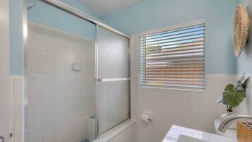 Ein Badezimmer mit Dusche, Toilette, Waschbecken und einem Fenster mit Jalousien.