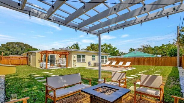 A backyard with a pergola, outdoor seating, a fire pit, and a house in the background.