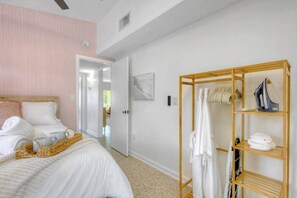 A bedroom with a bed, a wooden wardrobe, and a hallway leading to another room. - Surf Shack! Pool table! Fire Pit! 10 min to beach! (Martin County)