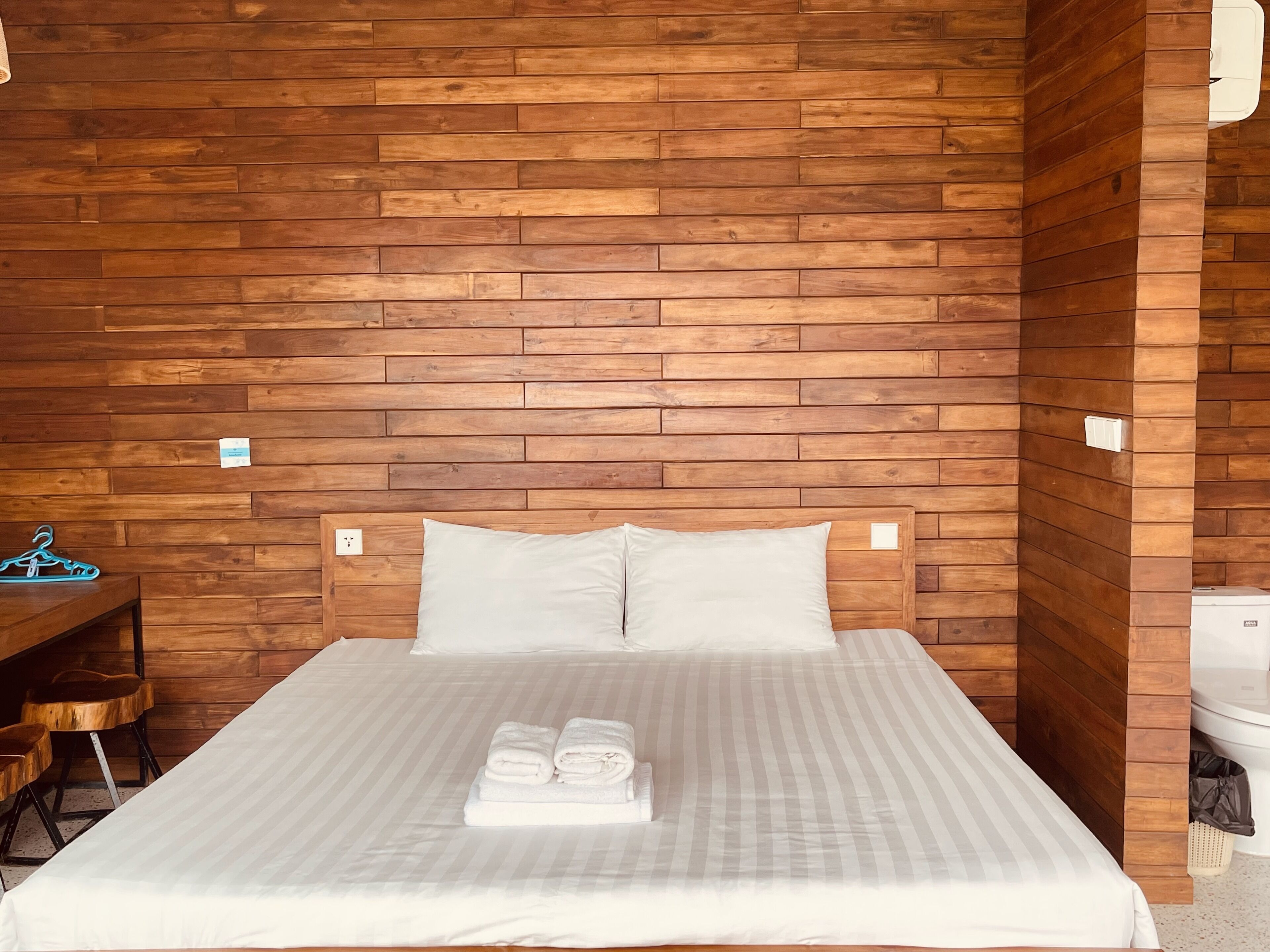 A hotel room with a wooden wall, a bed with white bedding, and a small desk with a chair.