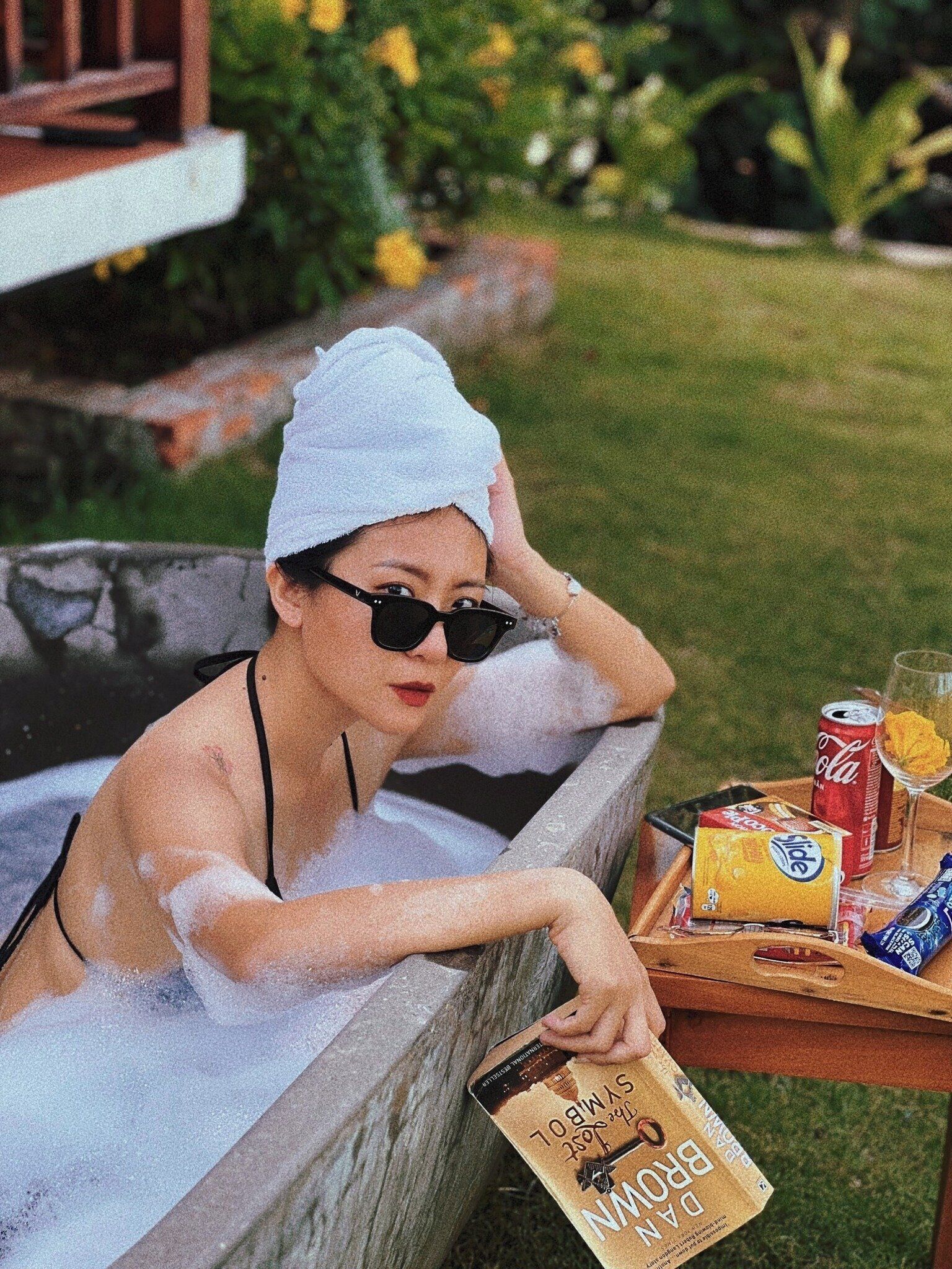 Una persona relajándose en un jacuzzi con una bandeja de bocadillos y bebidas.