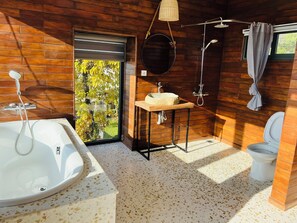 A modern bathroom with a freestanding bathtub, a sink with a stone countertop, a hanging mirror, and a toilet. - Lotus Home (Phu Quoc)