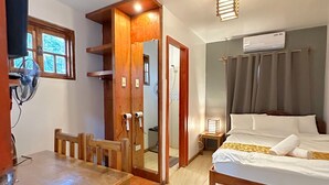 Habitación de hotel con cama de madera, una mesita con sillas, un espejo y ventana con persianas.