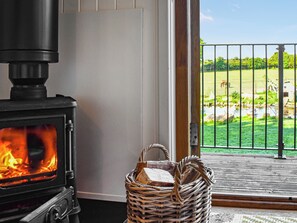 A wood-burning stove with a fire, a wicker basket with bread, and a view of a green landscape through a door.