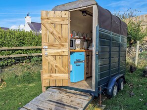 A small, wooden shed with a blue refrigerator inside, a door, and a ramp leading to the entrance.