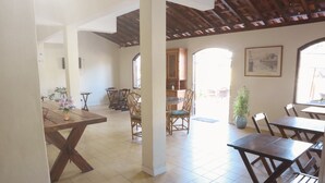 A spacious dining area with wooden tables and chairs, a tiled floor, and a view of the outside through large windows. - Pousada Lisamar (Mangaratiba)