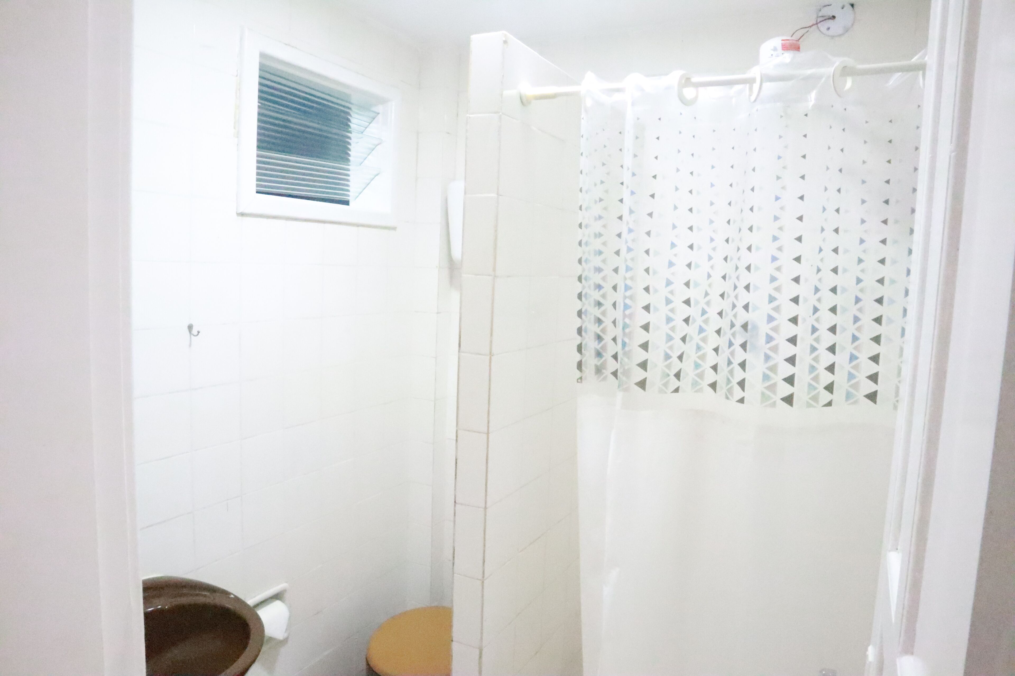 Un baño con inodoro, cortina de ducha y ventana con persianas.