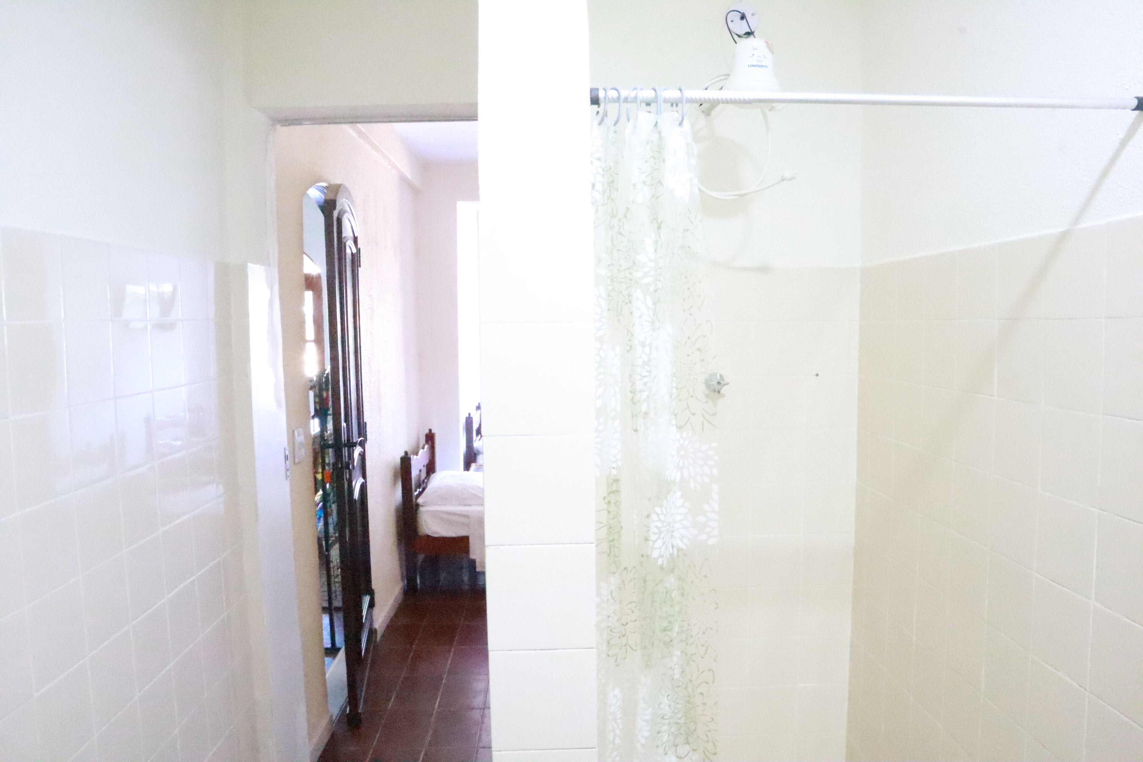 Ein Badezimmer mit weiß gefliesten Wänden, einer Duschvorhang und einer sichtbaren Toilette.
