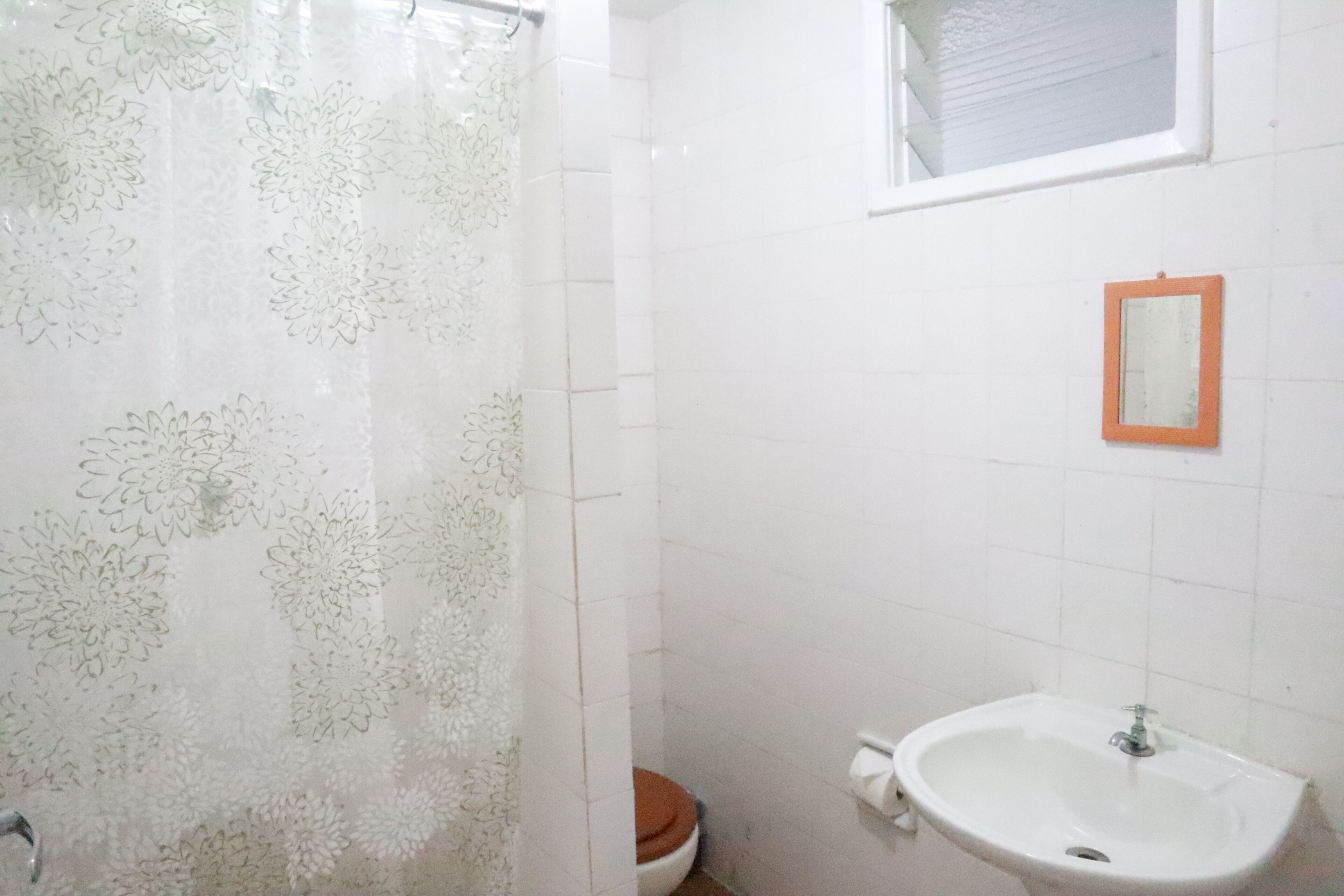 A bathroom with a shower curtain, toilet, sink, and a small mirror on the wall.