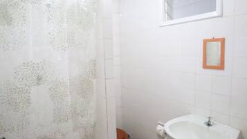 A bathroom with a shower curtain, toilet, sink, and a small mirror on the wall.