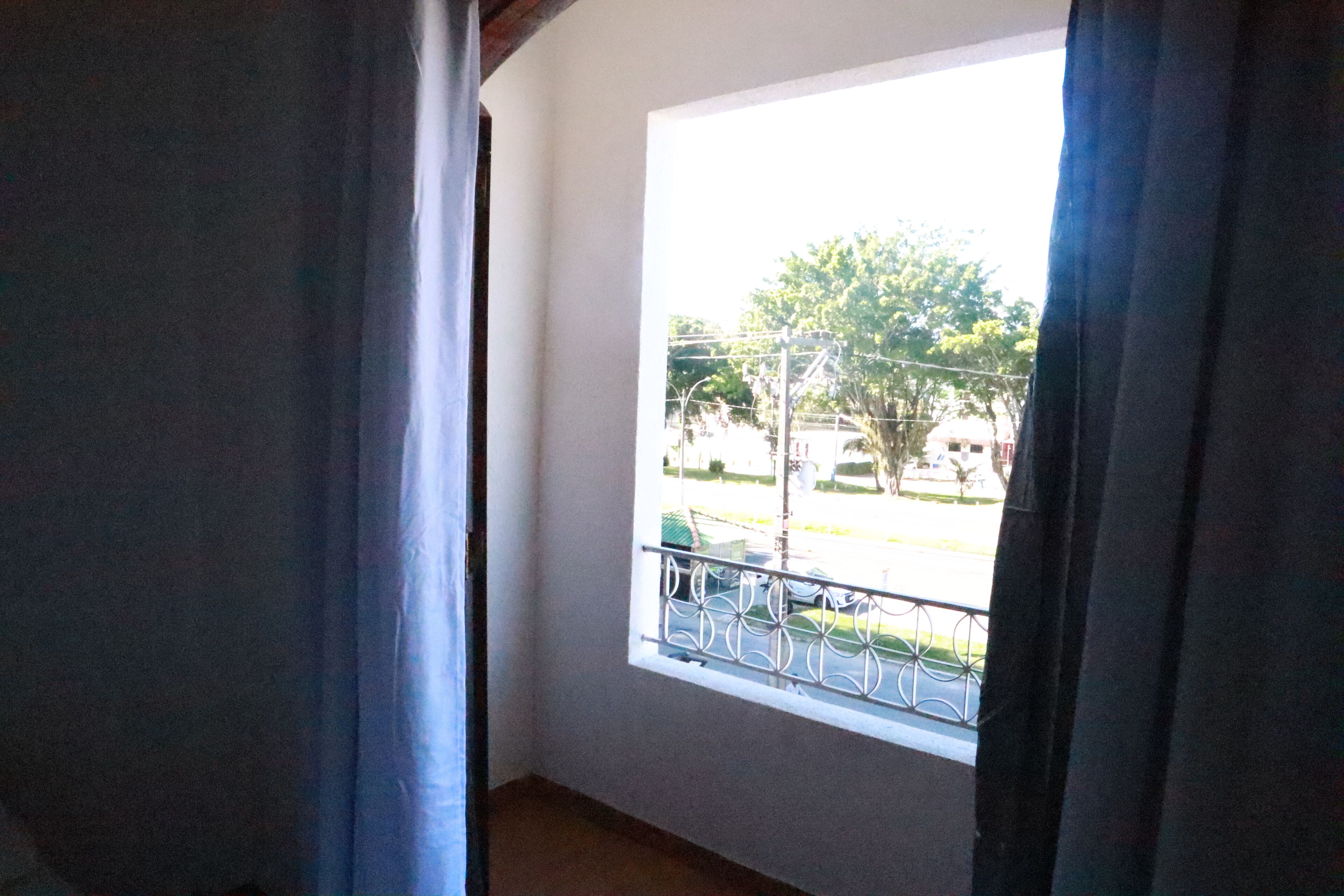 Una habitación con ventana que da a una calle con árboles y una valla.