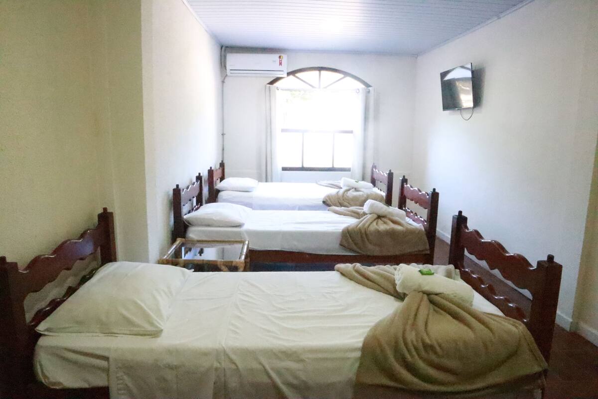 A room with three single beds, a small table, and a window with curtains.