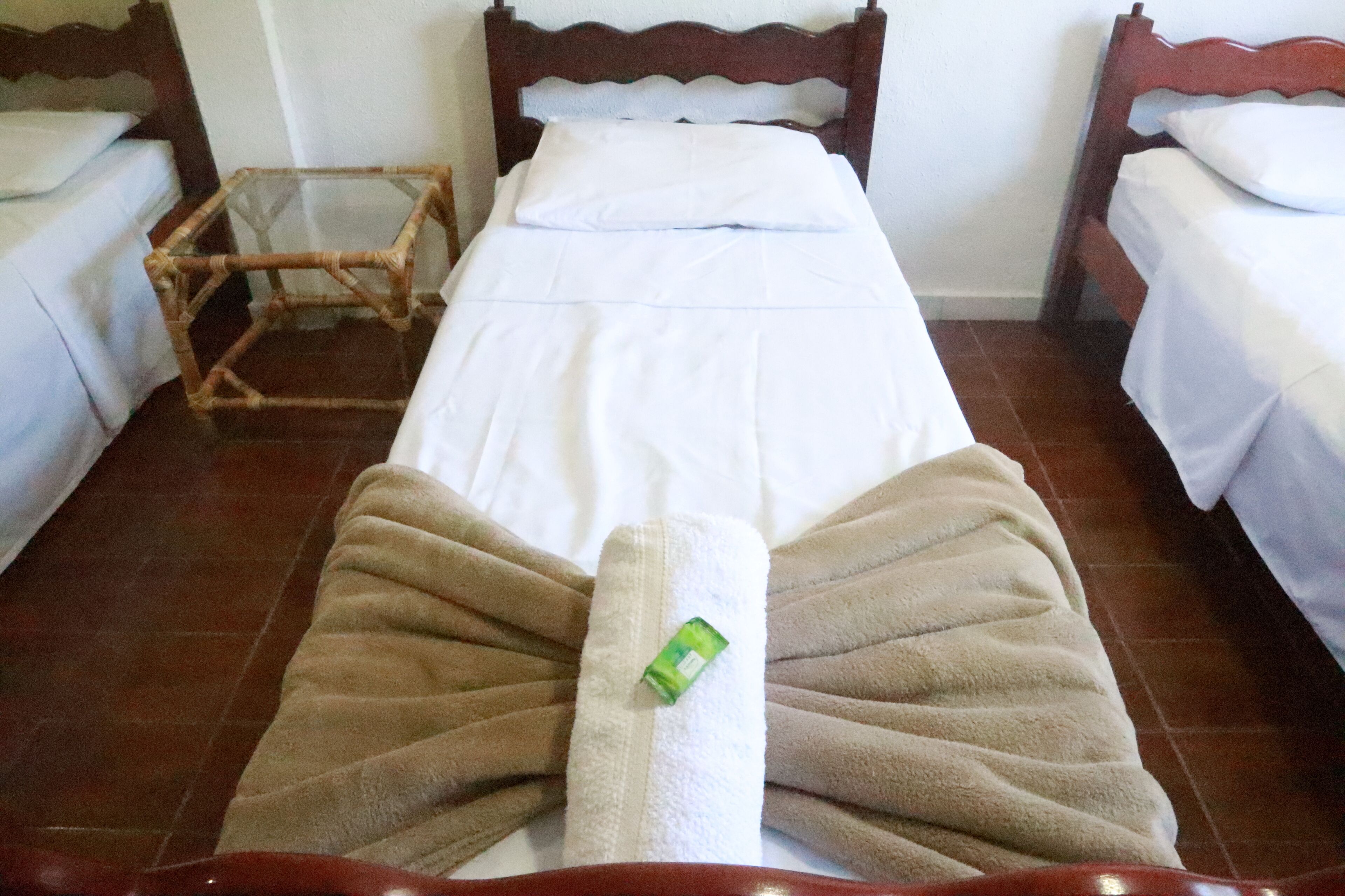 A hotel room with two single beds, a wooden headboard, a glass side table, and a brown towel on the bed.