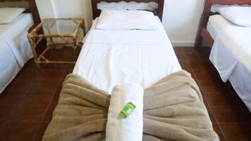 A hotel room with two single beds, a wooden headboard, a glass side table, and a brown towel on the bed.