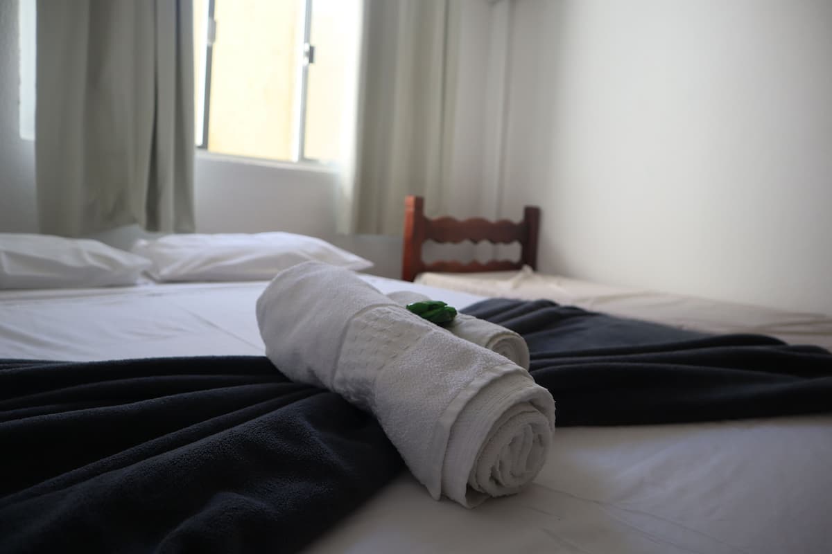 A neatly made bed with a rolled white towel and a dark blanket.