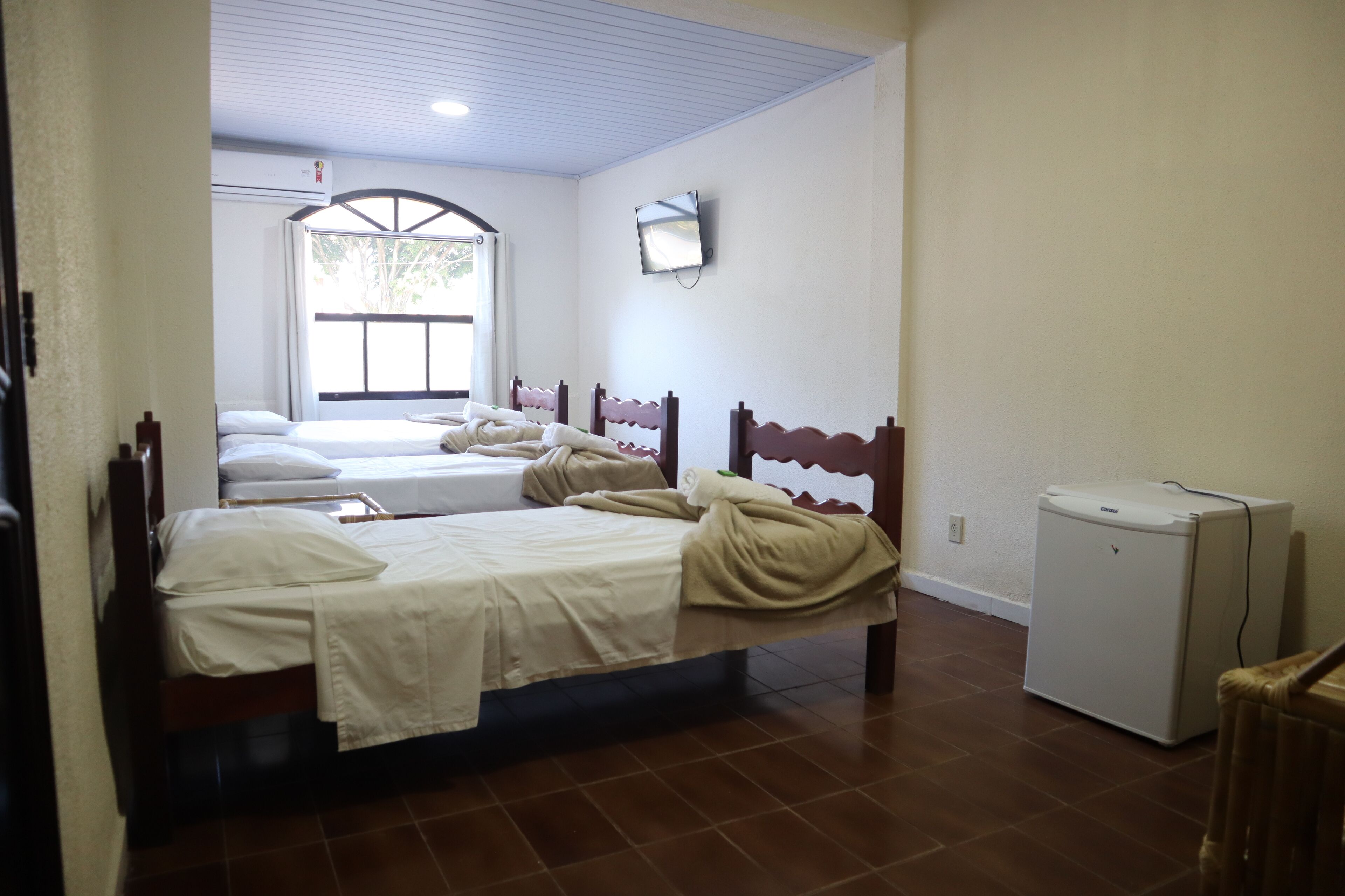 A hotel room with two beds, a small refrigerator, and a window with a view of greenery.