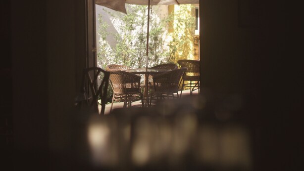 An outdoor seating area with wicker chairs and a table under a large umbrella, with greenery visible through the window. - Pousada Lisamar (Mangaratiba)