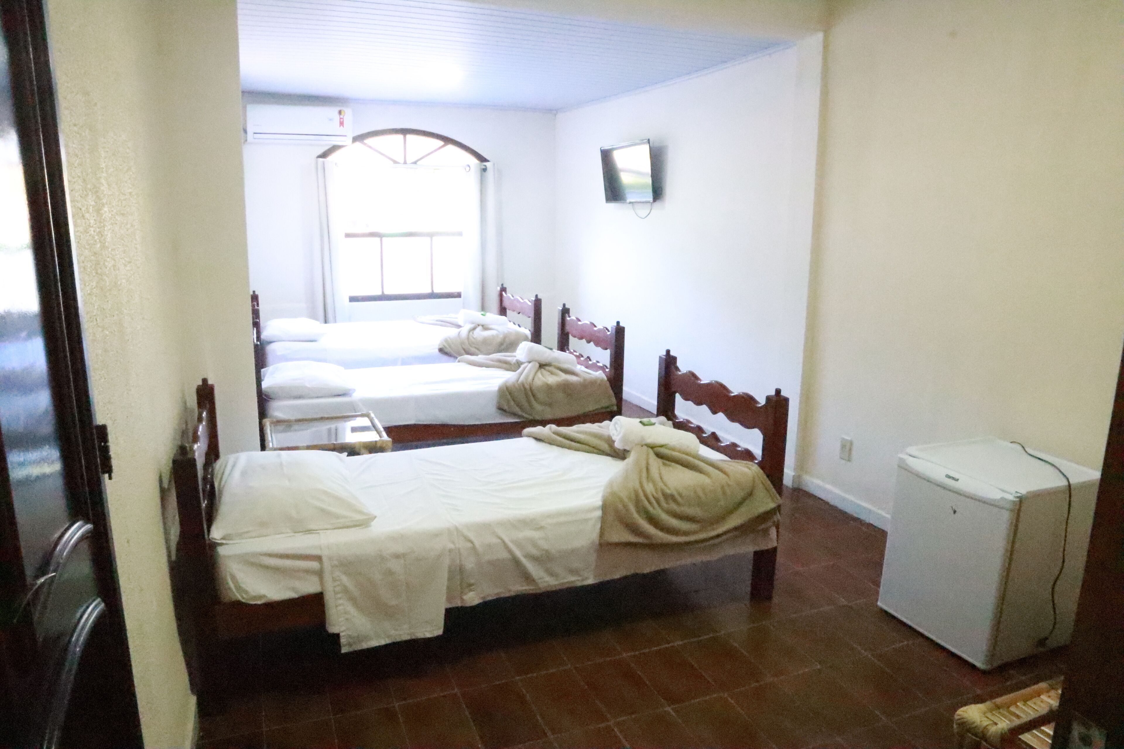 Quarto de hotel com duas camas, um pequeno frigorífico e janela com vista.