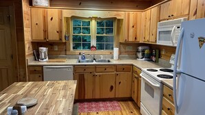 A kitchen with wooden cabinets, a microwave, a refrigerator, a sink, and a window with a view of greenery.