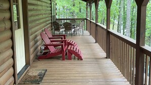 A wooden log cabin with a covered porch, featuring red Adirondack chairs and a dining table.