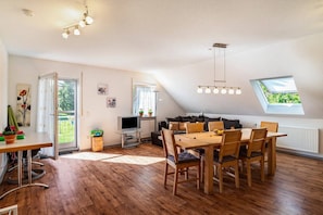 Amplia sala de estar con mesa de comedor, sillas, sofá y televisor. Una ventana ofrece luz natural y vistas al exterior.