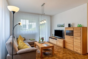 Un salon moderne comprenant un canapé, une table basse, un téléviseur, un meuble en bois et un lampadaire.