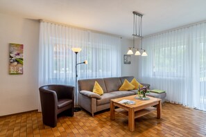 Un salon moderne comprenant un canapé, un fauteuil et une table basse, agrémenté d’un lampadaire et de rideaux légers.
