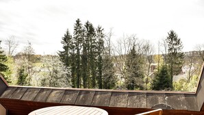 Eine Holzterrasse mit einem runden Tisch und einem Stuhl, mit Blick auf ein bewaldetes Gebiet.