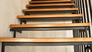 Eine hölzerne Treppe mit schwarzen Geländern führt zu einer weißen Tür.