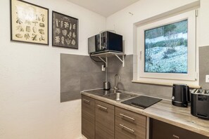 A kitchen with a sink, a microwave, a toaster, and a window with a view of a snowy landscape.